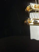 Close-up of a black guitar body with gold bridge hardware and strings visible against a dark background.