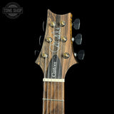 Close-up of a guitar headstock with a dark brown wood grain finish, six black tuning pegs, and a black pickguard with white 'Custom' lettering, shown against a black background with a Tone Shop watermark in the top left.