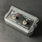 A Fender Power Musical Instruments Corp volume control module, model 007-37N DRIP00000, featuring a textured gray and black body with two metal footswitches on a dark gray surface.