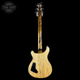 A single-cutaway electric guitar shown from the back, featuring a natural light wood body with a prominent black pickguard and a highly figured flame maple neck with a dark brown flame pattern, set against a solid black background.