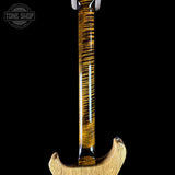 Close-up of the neck and lower body of an electric guitar with a glossy, highly figured wood finish showing dramatic brown and golden grain patterns, set against a solid black background.