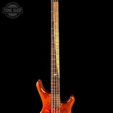 Close-up of a bass guitar with a dark background and 'Tone Shop' logo.