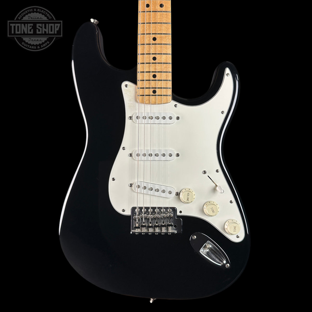 A black electric guitar with a white pickguard and a natural maple neck, shown against a solid black background. A Tone Shop watermark is visible in the top-left corner.