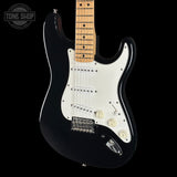 A black electric guitar with a white pickguard and maple neck, photographed against a solid black background. A Tone Shop watermark is visible in the top-left corner.