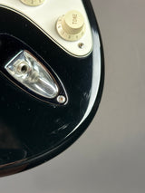 Close-up of a glossy black electric guitar body with a cream-colored control plate, tone knob, and chrome hardware against a neutral gray background.