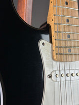 Close-up of an electric guitar showing the black body, silver pickguard, maple fretboard, and strings.