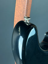 Close-up of a glossy black guitar body with a visible metal tailpiece and a small scratch on the surface, against a dark gray background with a brown wood element at the left.