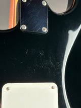 Close-up of a glossy black electric guitar body showing a worn black pickguard with visible scratches and a white pickguard plate with screws.
