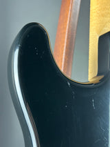 Close-up of a glossy black guitar body with visible scuffs and scratches on the finish, showing part of a gold headstock and a wooden neck joint in the background.