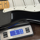 A close-up of an electric guitar body resting on a digital scale, showing the scale reading 7.77 kg.