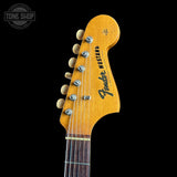 Close-up of the headstock of a Fender Mustang electric guitar against a solid black background, showing the yellow-orange maple headstock, six silver tuning pegs, and black Fender branding.