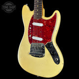 A classic electric guitar with a cream-colored body, a red glittery pickguard, and a black control plate, shown against a solid black background.