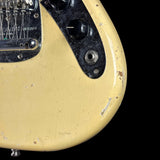 Close-up of a distressed cream-colored electric guitar body with black control plate and hardware, showing worn paint details against a black background.
