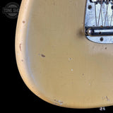 Close-up of the lower bout corner of a vintage electric guitar body, featuring a heavily worn, distressed cream or light tan finish with scuffs and peeling paint, alongside a chrome hardware bridge.