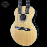 Acoustic guitar with a black pickguard on a black background, featuring the Tone Shop logo.