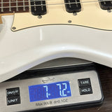 A close-up of a white electric guitar body resting on a digital kitchen scale displaying 7.12 lbs.