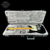 A black electric guitar with a yellow neck and headstock, displayed inside an open gray hard case with a textured gray insert. The case is set against a solid black background, with a 'TONE SHOP' watermark in the upper left corner.