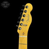 Close-up of a Fender Telecaster electric guitar headstock in a natural maple finish, showing six black tuning pegs and the Fender logo, set against a solid black background.