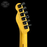Close-up of the headstock of a yellow electric guitar against a black background, showing six black tuning pegs and a Tone Shop watermark in the upper left corner.