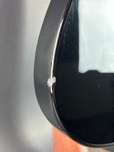 Close-up of a black glossy curved surface with a small clear adhesive or resin dot near the lower edge, against a neutral gray background.