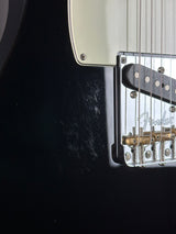 Close-up of a black electric guitar body showing part of the cream pickguard, silver hardware, and a Fender logo on the bridge plate.