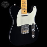 A black electric guitar with a cream pickguard, maple neck, and chrome hardware, shown against a solid black background with a Tone Shop watermark in the top-left corner.