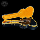 Acoustic guitar in a black case with orange interior, Tone Shop logo visible.