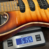 Close-up of a guitar body resting on a digital scale showing 6.15 oz, with the scale brand Weld Max visible.