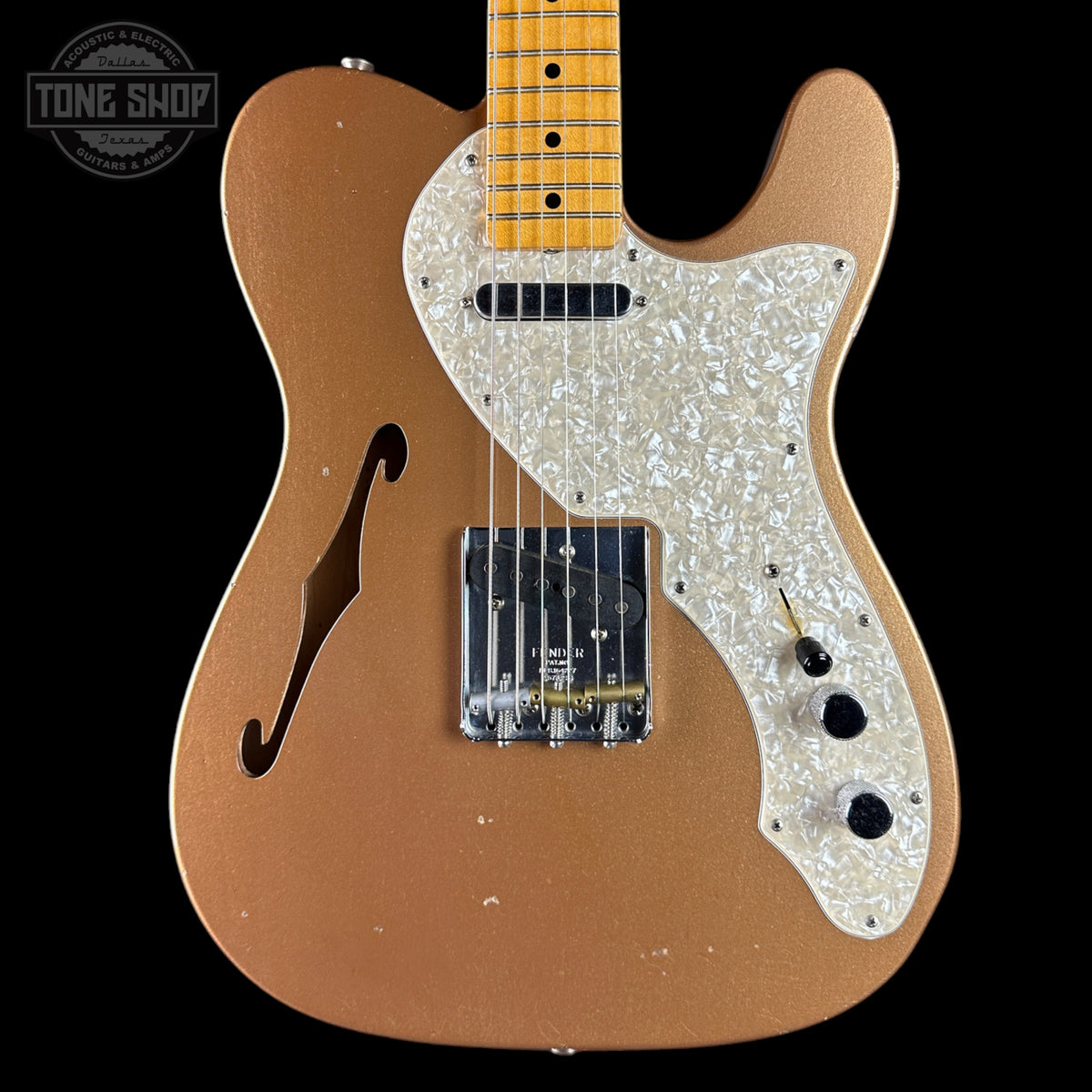 Electric guitar with a brown body and white pickguard on a black background, featuring 'Tone Shop' branding.