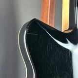 Close-up of the upper bout corner of a glossy black electric guitar body, showing visible scratches on the finish and a thin light-colored edge stripe against a dark gray background.