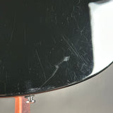Close-up of a glossy black curved surface with visible scratches and scuffs, showing a small silver screw or fastener near the bottom edge.