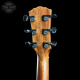Close-up of the headstock of a wooden guitar, showing six black tuning pegs with silver rings and the brand name 'Tone Shop' printed on each peg. The wood has a warm brown finish with visible grain, set against a solid black background.