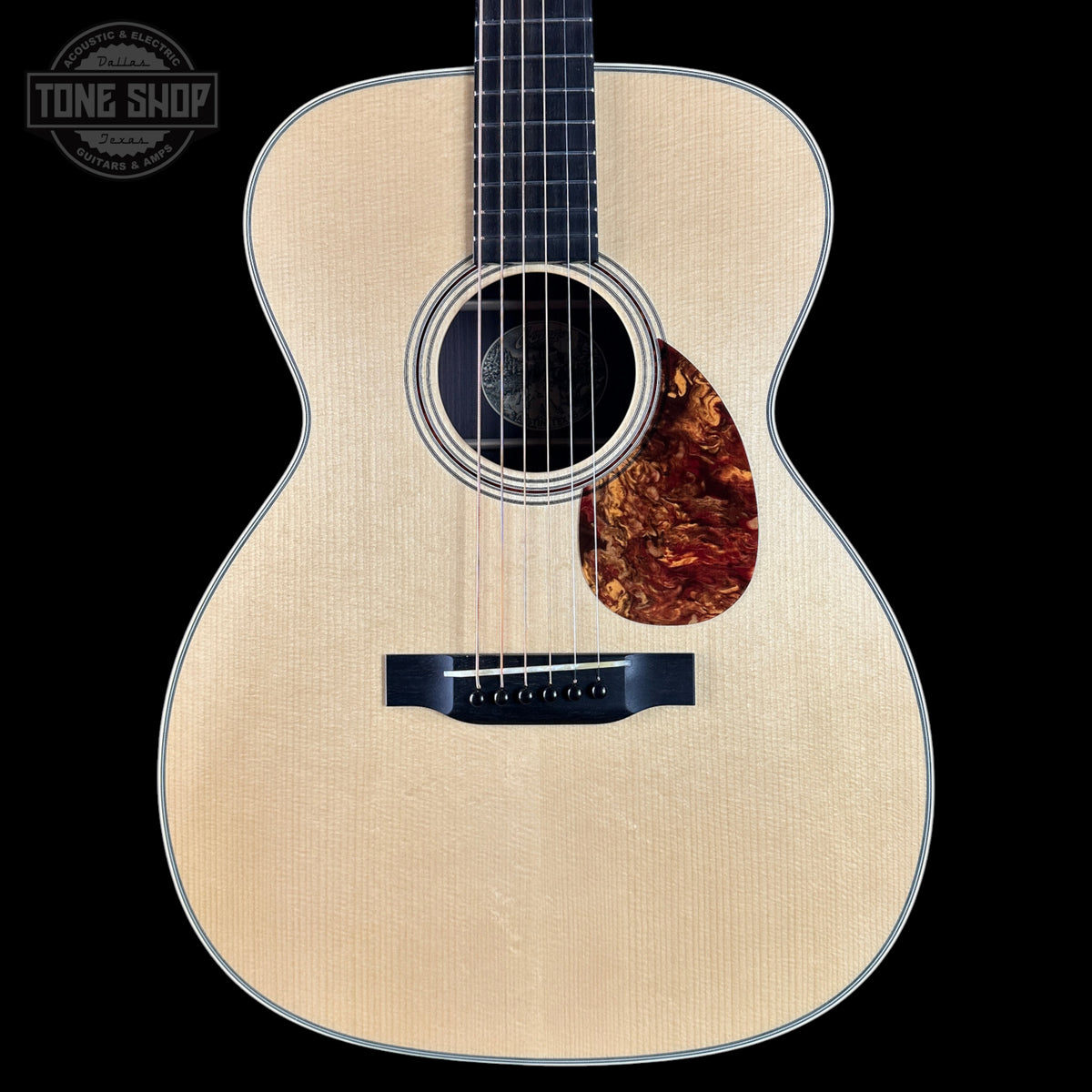 Acoustic guitar with a tortoiseshell pickguard on a black background, featuring the Tone Shop logo.