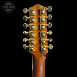 Close-up of a double-neck guitar headstock with twelve gold-toned tuning pegs on a dark brown wood finish, set against a solid black background.