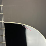 Close-up of the edge of a glossy black guitar body with a visible red scratch on the varnish, next to the neck.