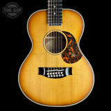 A vintage-style acoustic guitar with a natural sunburst finish, black pickguard, and a decorative tortoiseshell-style pickguard overlay, shown against a solid black background.