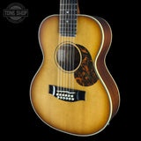 A 12-string acoustic guitar with a natural sunburst finish, black bridge, and a decorative tortoiseshell-style pickguard, shown against a solid black background with a Tone Shop watermark in the top-left corner.