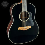 A close-up studio shot of an acoustic guitar body against a black background, showing a glossy black finish, white binding, a natural wood bridge, and part of the neck. A Tone Shop watermark is visible in the upper left corner.