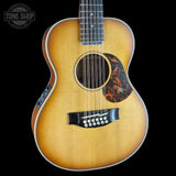 An acoustic guitar with a natural sunburst finish, featuring a black 12-string bridge and a decorative tortoiseshell pickguard, shown against a solid black background.
