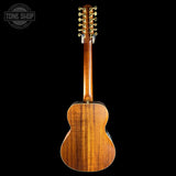 The back view of a wooden acoustic guitar with a glossy finish, showcasing its rich grain and six gold tuning pegs, set against a solid black background with a Tone Shop watermark in the top left corner.