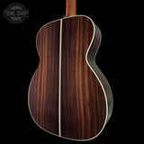 Back view of a wooden acoustic guitar with a visible brand logo in the corner.