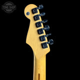 Close-up of the headstock of a Fender electric guitar in a natural maple finish, showing six black tuning pegs with Fender logos, set against a solid black background with a Tone Shop watermark in the top left corner.
