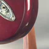 Close-up of a glossy dark red electric guitar body with a chrome hardware piece and a small visible scratch on the finish, photographed against a soft gray background.