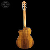 A classical acoustic guitar shown from the back, featuring a rich wood grain body and neck, set against a solid black background with a Tone Shop watermark in the top left corner.