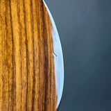 Close-up of a polished wooden object with prominent grain, showing a warm golden-brown surface and a curved edge against a dark gray background.