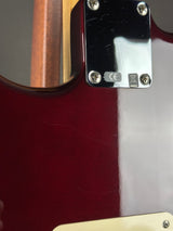 Close-up of an electric guitar body showing a glossy dark red finish, a black hardware plate with screws, and part of a cream pickguard.