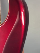 Close-up of a glossy metallic deep red guitar body showing the upper bout curve and a small portion of the neck joint against a neutral gray background.