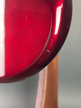Close-up of a glossy deep red curved surface, likely part of a product, with a soft gray background and a brown horizontal element behind it.