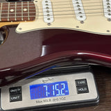A close-up of a guitar body resting on a digital scale, showing the scale reading 7.152 oz.