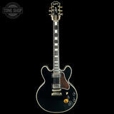 A black Gibson Les Paul Custom electric guitar with gold hardware, shown vertically against a solid black background. The Gibson logo is visible on the headstock, and a Tone Shop watermark is in the top-left corner.